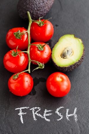 Closeup of fresh tomatoes and avocados with word fresh written in chalk on dark backgroundの写真素材