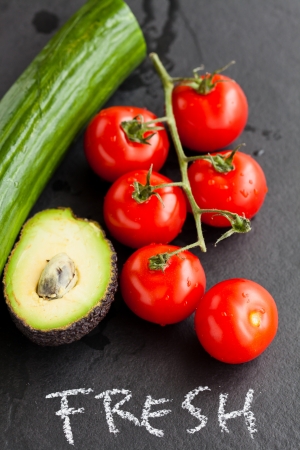 Closeup of fresh tomatoes and avocado half and cucumber with word fresh written in chalk on dark backgroundの写真素材