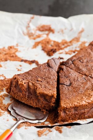 Freshly baked homemade chocolate cake slices with cake server utensil on baking paperの写真素材