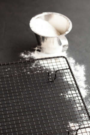 Mesh tray and flour in metal measuring cup and spread on dark backgroundの写真素材