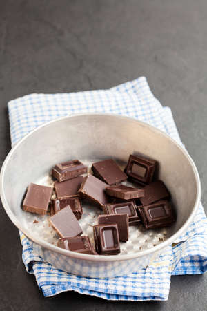 Closeup of bowl containing pieces of chocolate resting on blue checkered napkin on dark backgroundの写真素材