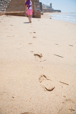 Young girl walking on beach at Areia Branca Portugal with footprints in foregroundの写真素材
