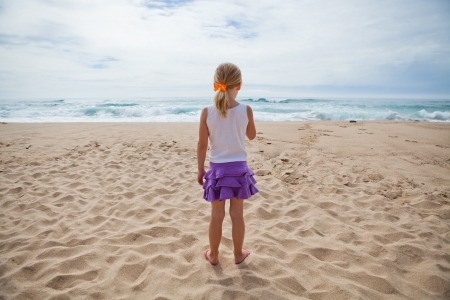 Young girl standing at beach in sand and looking towards oceanの写真素材