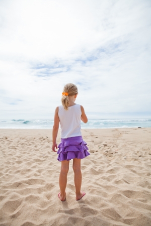 Young girl standing at beach in sand and looking towards oceanの写真素材