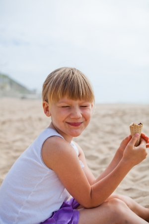 Young happy smiling girl sitting on beach with half eaten ice cream coneの写真素材