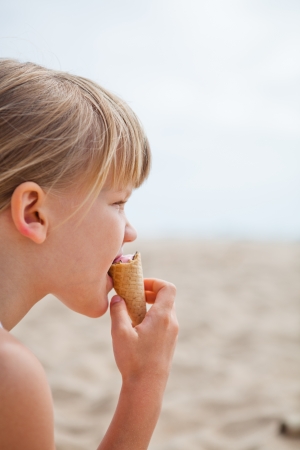 Young cute girl eating ice cream while at beachの写真素材