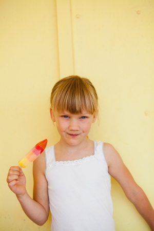 Smiling young girl with multicolored sweet against yellow colored backgroundの写真素材
