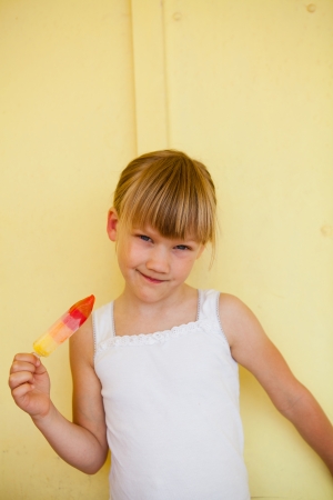 Smiling young girl with multicolored sweet against yellow colored backgroundの写真素材