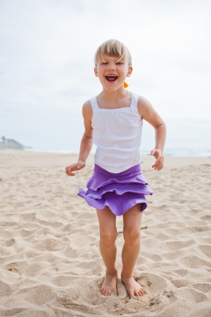 Happy barefoot young girl in purple skirt and white top playing on beachの写真素材