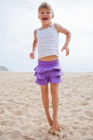 Happy barefoot young girl in purple skirt and white top jumping in sand on beachの写真素材