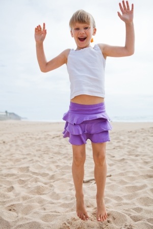 Happy barefoot young girl in purple skirt and white top jumping in sand on beachの写真素材