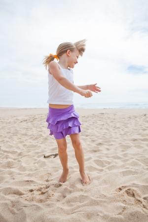 Happy barefoot young girl in purple skirt and white top playing on beachの写真素材