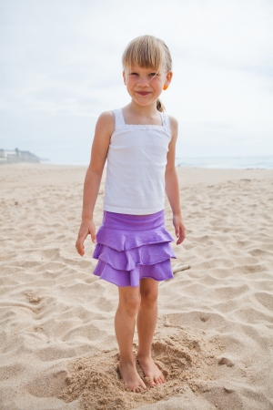 Happy and smiling barefoot young girl in purple skirt and white top at beachの写真素材