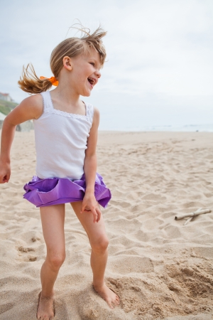 Happy barefoot young girl in purple skirt and white top playing on beachの写真素材