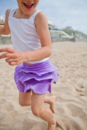 Closeup of happy barefoot young girl in purple skirt and white top playing on beachの写真素材
