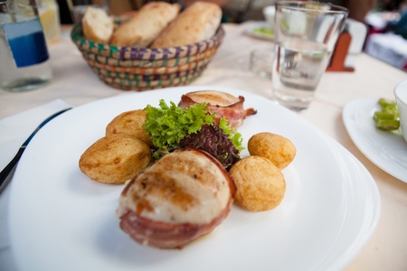 Closeup of grilled chicken breast wrapped in bacon with sides of baked potatoes and saladの写真素材