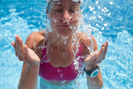 Happy female swimmer splashing water in face with eyes closed while in swimming poolの写真素材