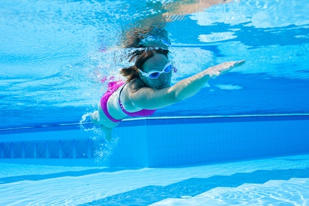 Underwater view of female with violet swimsuit and white goggles swimming in poolの写真素材