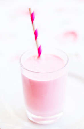 Closeup of raspberry smoothie made with milk and ice cream and with striped white and pink straw in glass on light backgroundの写真素材