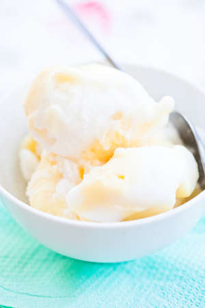Closeup of scoops of vanilla ice cream and spoon in white bowl on light backgroundの写真素材