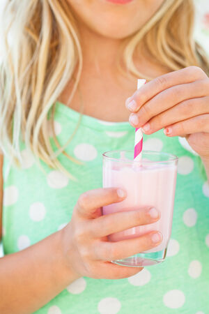 Closeup of glass of smoothie drink with straw held in hand by young girlの写真素材