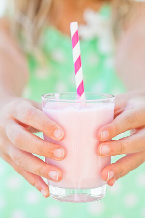 Closeup of glass of smoothie drink with straw held in hands by young girlの写真素材