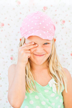 Portrait of cute smiling young girl looking through one eye while covering other eye with fingersの写真素材