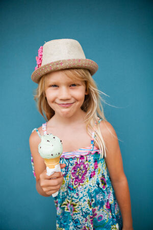Cute smiling young girl holding ice cream cone outside against blue wall backgroundの写真素材