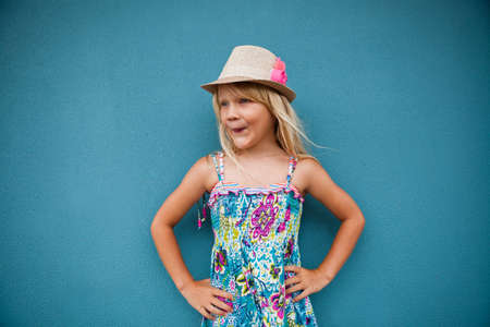 Portrait of stylish cute young girl with funny expression outside against blue wall backgroundの写真素材