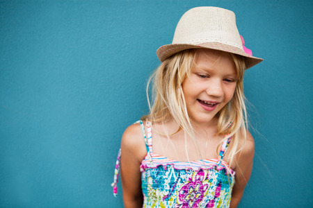 Portrait of stylish cute young girl smiling outside against blue wall backgroundの写真素材