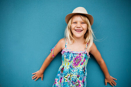 Portrait of stylish cute young girl smiling outside against blue wall backgroundの写真素材