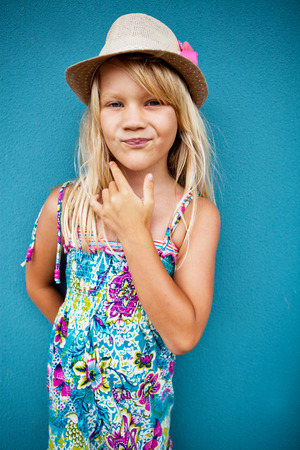 Portrait of stylish cute young girl with smirk expression outside against blue wall backgroundの写真素材