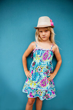 Portrait of serious looking cute young girl wearing stylish hat outside against blue wall backgroundの写真素材