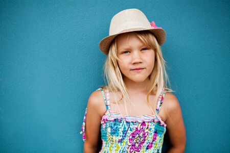 Portrait of cute young girl in relaxed pose wearing stylish hat outside against blue wall backgroundの写真素材