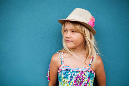 Portrait of cute young girl wearing stylish hat and looking to side outside against blue wall backgroundの写真素材