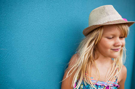 Cute young girl wearing stylish hat smiling outside against blue wall backgroundの写真素材