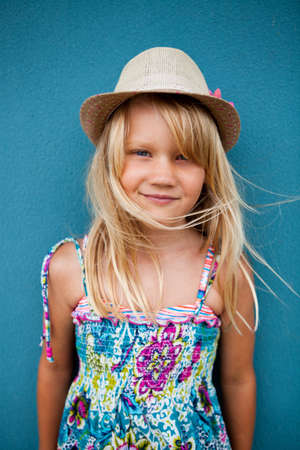 Portrait cute happy young girl wearing stylish hat outside against blue wall backgroundの写真素材