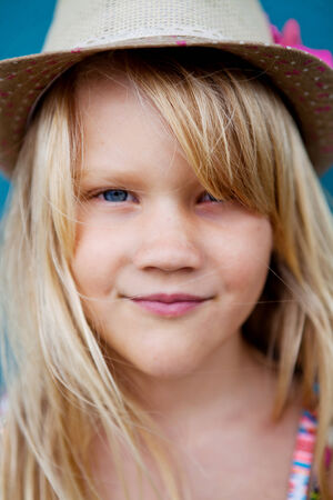 Closeup of face of cute smiling young girl with stylish hat outside against blue wall backgroundの写真素材