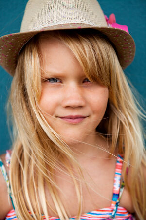 Closeup portrait of cute young girl with stylish hat outside against blue wall backgroundの写真素材