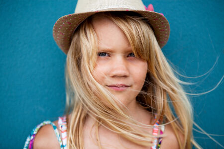 Closeup portrait of cute young girl with stylish hat outside against blue wall backgroundの写真素材
