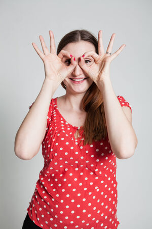 Studio portrait of smiling attractive woman looking through finger gogglesの写真素材