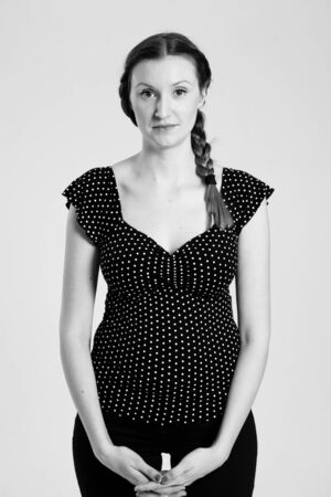 Black and white studio portrait of attractive woman with pigtail holding hands togetherの写真素材