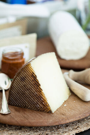 Closeup of piece of cheese and condiment in jar on wooden cutting board with cheese in backgroundの写真素材