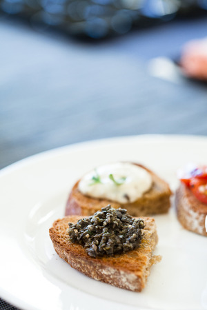 Closeup of bruschetta appetizers with savoury paste and mozzarella cheese toppings on white plateの写真素材