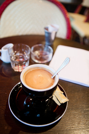 Closeup of cup of espresso coffee with metal spoon on wooden cafe table with glass of water and small jug and ashtray in backgroundの写真素材