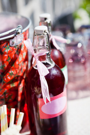 Closeup of two bottles of strawberry based fruit juice with decorative ribbons and labels on table at outdoors party in sunlightの写真素材