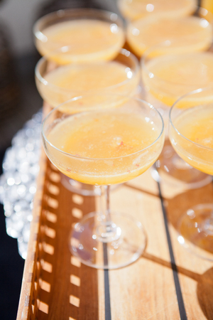 Closeup of glasses of orange juice in rows on wooden serving tray at outdoor party in sunlightの写真素材
