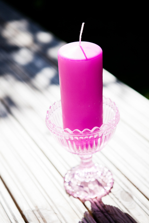Closeup of decorative purple candle in glass stand resting on table outdoors on sunny dayの写真素材