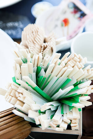Closeup of bunch of wooden chopsticks on table outdoors ready for use at party with forks in backgroundの写真素材