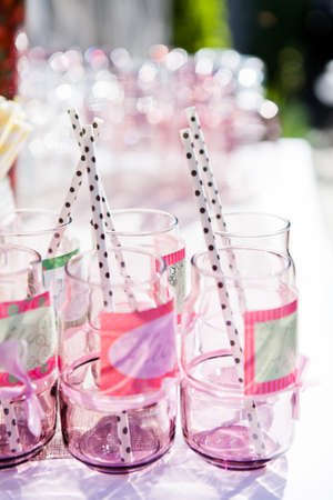 Closeup of decorative pink colored party glasses with straws and labels on table outdoors on bright dayの写真素材